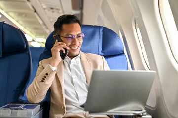 Successful Asian businessman looks at his laptop screen, on the phone during the flight