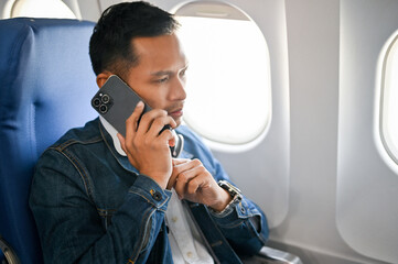 Handsome Asian man is on the flight to hometown, talking on the phone before take off.