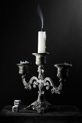 Candles in holder with smoke and a pair of dices still life in dramatic light - 555358201