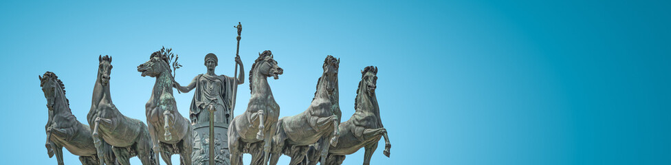 Fototapeta na wymiar Banner with statue of Goddess Victoria with horses at the top of Triumphal Arch called Arch of Peace in Milan historical downtown, Sempione Park, Italy, at blue sky gradient background with copy space