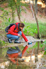 Young female hiker filling water bottle of raw water in a creek.