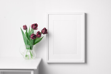 Blank portrait frame mockup on white wall with tulip flowers in vase