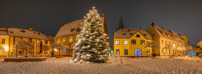 Panorama view of market square with decorated Christmas tree covered with snow on winter day. ...
