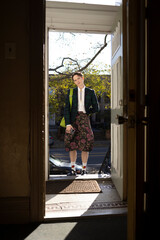 fashionable non-binary person wearing jacket and skirt in doorway