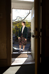 fashionable non-binary person wearing jacket and skirt in doorway