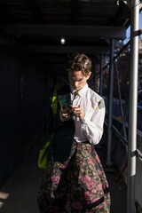 non-binary young person using smartphone in dramatic sunlight and shadow