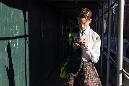 non-binary young person using smartphone in dramatic sunlight and shadow