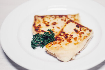 thin pancakes with meat filling and a sprig of parsley on a white plate