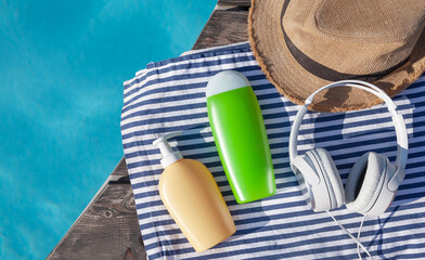 Cosmetic bottles, headphones and sun hat near swimming pool