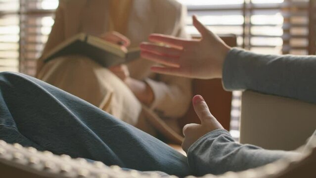 Selective focus slowmo of unrecognizable young woman sitting in chair speaking about her feelings and problems during psychotherapy session
