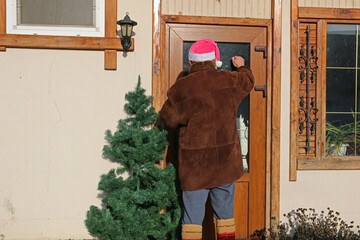 A man in a Santa Claus hat brought a Christmas tree into the house.