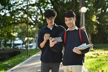 Two asian students talking to each other after classes while walking in university campus outdoors