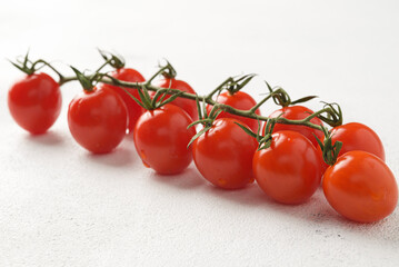 Bunch of red cherry tomatoes with green leaves on light background