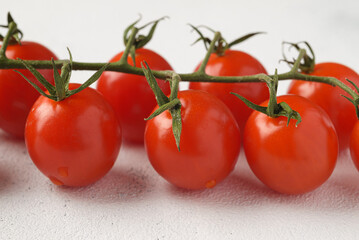 Bunch of red cherry tomatoes with green leaves on light background