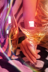 The girl is holding a martini glass, sitting on a zebra skin, her hand is holding a glass. Festive background, multi-colored glare of lights, party.