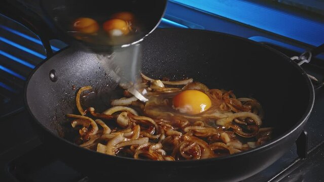 Adding eggs to a frying pan with fried onion on it, close up view.