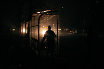Fototapeta na wymiar Men on the buss stop in full dark in the headlights. Streets without street lighting.