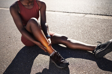 Leg, injury and pain with a sports black woman holding her ankle outdoor during a fitness workout from above. Ankle, sprain or exercise with a female runner or athlete suffering from an injured joint