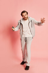 Active happy man with beard wearing home sportswear doing exercises isolated over pink background. Concept of active lifestyle, positive emotions, sport