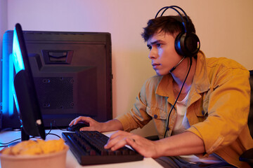 Serious young man wearing headset when playing videogame at home © DragonImages