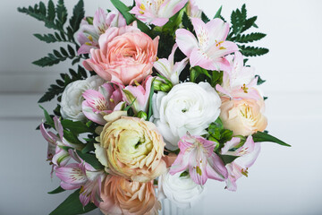 Beautiful bouquet of fresh colorful pastel ranunculus and lily flowers in full bloom with green fern leaves against white background, close up. Spring bunch of blossoms.