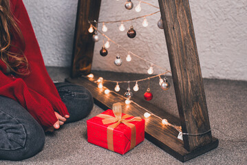 The girl is sitting near the Christmas tree decorated with toys and garlands. A gift for Christmas