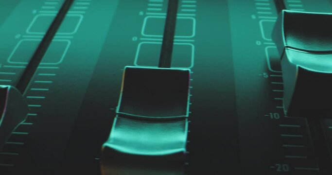 Extreme close-up camera pan over individual faders of audio mixer in colorful pulsating light of party