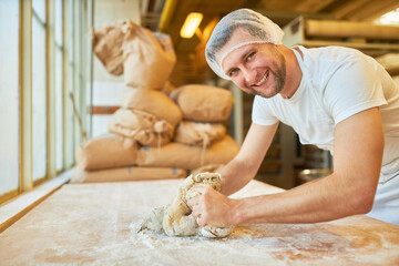 Happy young man baker apprentice kneading dough - obrazy, fototapety, plakaty