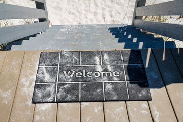 Destin, Florida- Black welcome mat with white sand on top of a wooden stairs