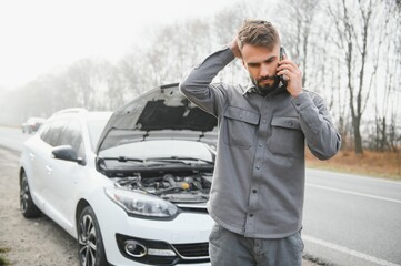 Man use a cellphone call garage in front of the open hood of a broken car on the road in the...