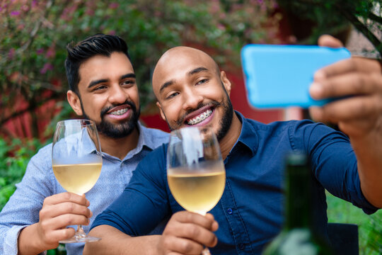 romantic gay couple taking selfie with mobile and glass of wine outside in the garden