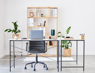 Empty office, table or desk in a home office interior or office desk with pens, plants or stationery for productivity. Furniture, chair or modern office room with laptop or folders in a wooden shelf