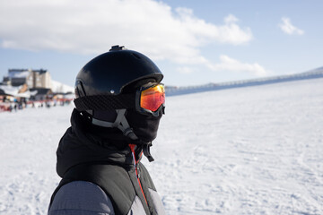 Girl or boy in ski helmet, sunscreen mask and balaclava close up stands against the backdrop of snow-covered mountain ski slope and a cloudy sky. Winter. Sport and travel content  