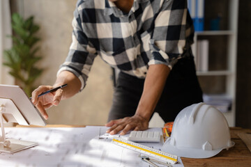 business man hand working and laptop with on on architectural project at construction site at desk in office.