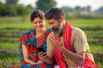 Indian farmer with wife using smartphone at agriculture field.