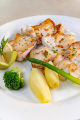 Fried monkfish with vegetables and lemon on a white plate