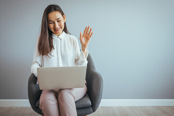 Happy asian young business woman, looking at computer screen, waving hello. Pleasant attractive mixed race female professional holding video call with client. Young woman having video call