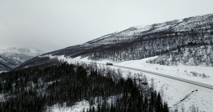 Isolated truck driving along E8 highway in winter season with valley shrouded in mist on background, Norway. Aerial drone panoramic view. Sky for copy space