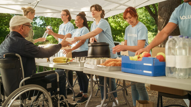 Group of Volunteers Helping in a Local Community Food Bank, Handing Out Free Food to People in Need in a Park on a Sunny Day. Man with Disabilities Using Wheelchair is Thankful for Charity Meal.