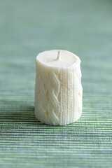 White candle with a knitted pattern on a green background. Soft focus. Photo