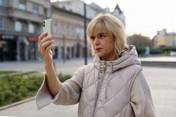 Portrait of tense Caucasian woman makes video call on her smartphone at street. Concept of online...