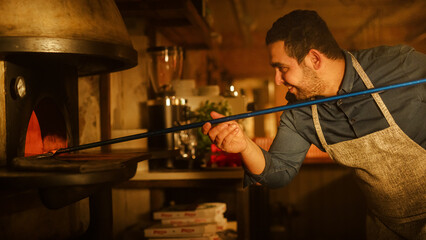 In Restaurant Professional Chef Uses Pizza Peel for Transferring Pizza into Wood Fire Stone Oven. Traditional Italian Cooking Family Recipe. Authentic Pizzeria, Delicious Organic Food. Cinematic Shot