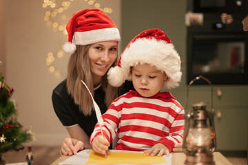 Fototapeta na wymiar Mom and kid write wishlist to Santa, Happy family holiday, Christmas Eve at home