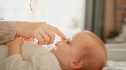 Close Up Portrait of a Loving Young Beautiful Mother Playing and Soothing Adorable Baby in Bed. Smiling Caring Mom and Cute Little Infant Child Cuddling in Bedroom. Motherhood Tender Moments.