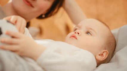 Caring Mother Lying on a Bed, Playing with a Cute Newborn Baby at Home. Mom Bonding with a Toddler, Baby Holding a Soccer Ball. Concept of Childhood, New Life, Motherhood.