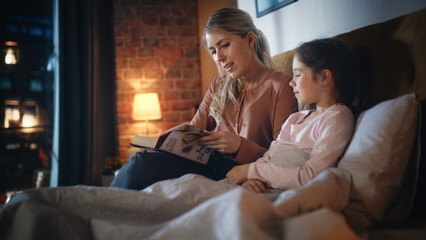 Mother Reading a Fairytale to Her Lovely Small Daughter in Bed Before Going to Sleep. Young Beautiful Mom Caring for Little Girl, Reading Stories from a Book in the Evening at Home.