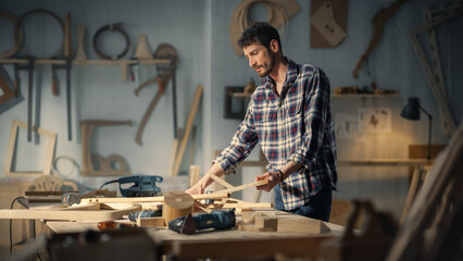 Young Carpenter Reading Blueprints and Starting to Assemble Parts of a Wooden Chair with a Rubber Hammer. Stylish Furniture Designer Working in a Studio in Loft Space with Tools on the Walls.