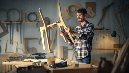 Young Stylish Carpenter Assembling Parts of a Wooden Chair. Professional Furniture Designer Working in a Studio in Loft Space with Tools on the Walls