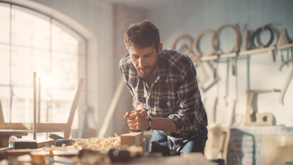Close Up Portrait of a Handsome Young Artisan Craftsman in Checkered Shirt Using Hand Plane to Shape a Wood Bar. Carpenter Working on a Project in a Loft Studio with Tools on Walls.
