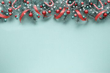 Christmas garland, border, banner with fir twigs, ribbons, candy canes, garland, frosted red berries and trinkets. Top view, flat lay, festive Xmas background on mint blue. Copy-space, place for text.